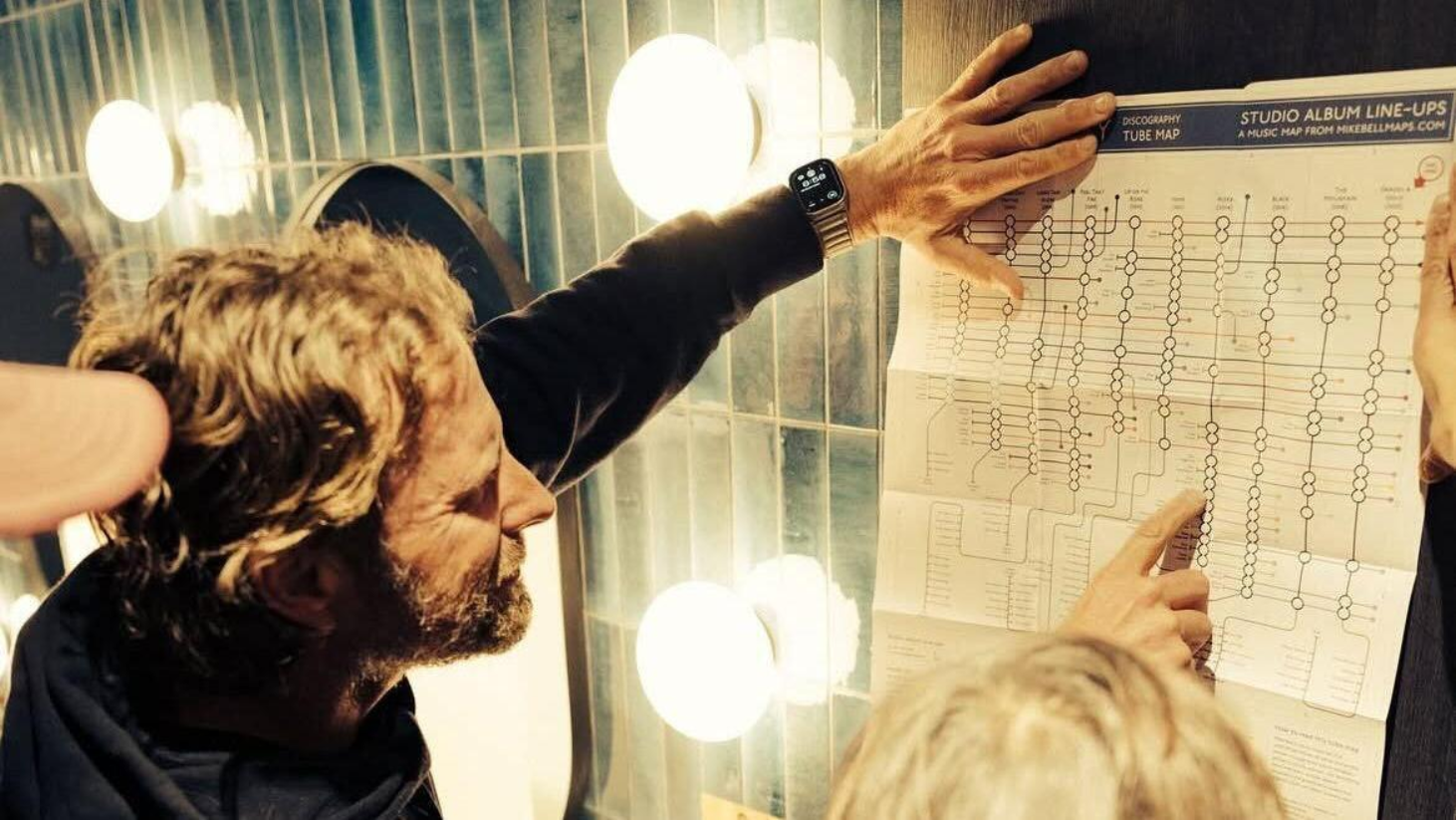 Dierks Bentley is holding a discography Z-fold tube map of his albums  in a room with lights.